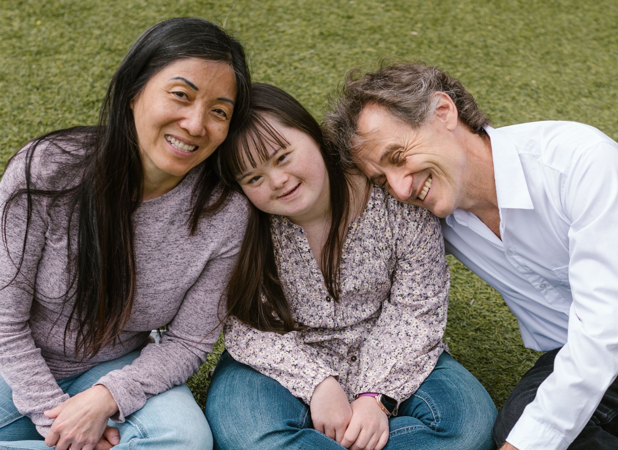 mother, daughter with down syndrome, and father smiling and sitting closely together