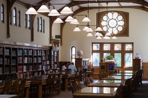 2 adults seated at table in library working together