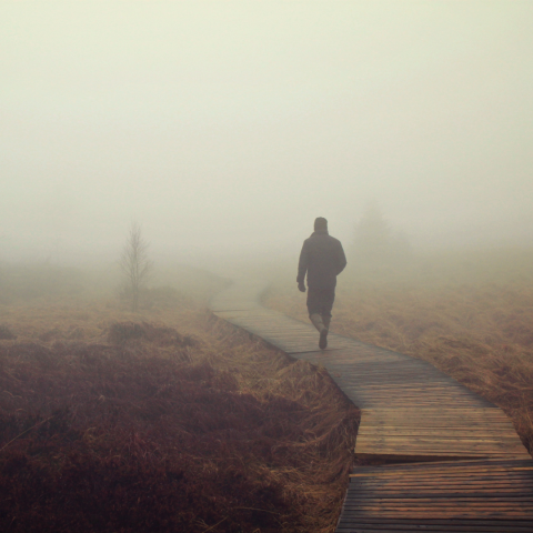 man walking on bridge in the fog