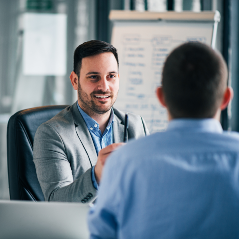 one man sitting across desk from another, having meeting
