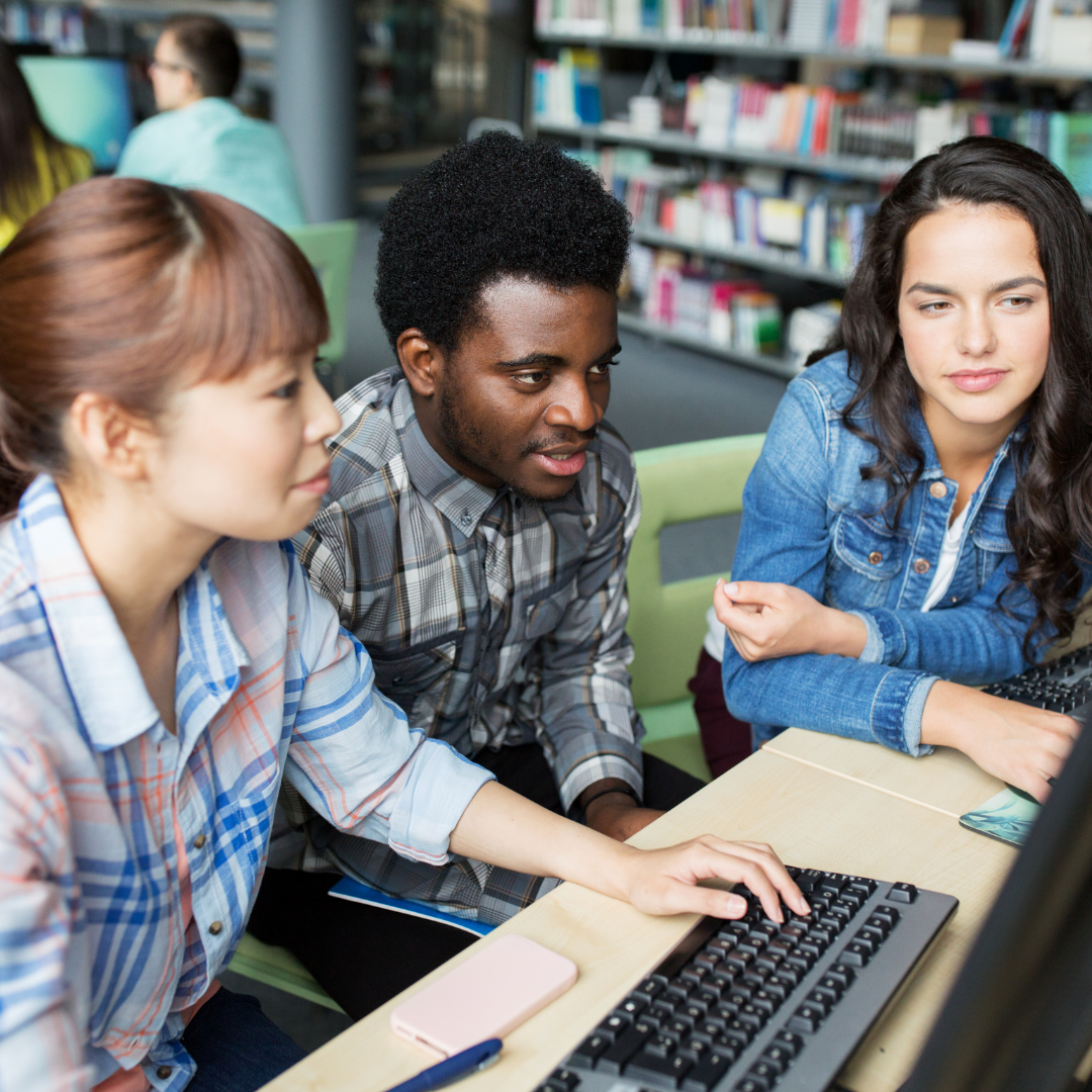 three teenagers huddle work together on a computer at the library